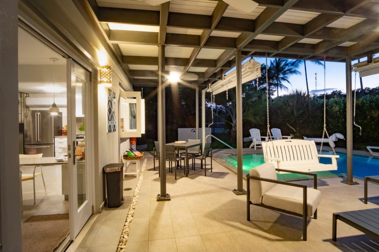 Covered terrace at dusk with swing and lit pool
